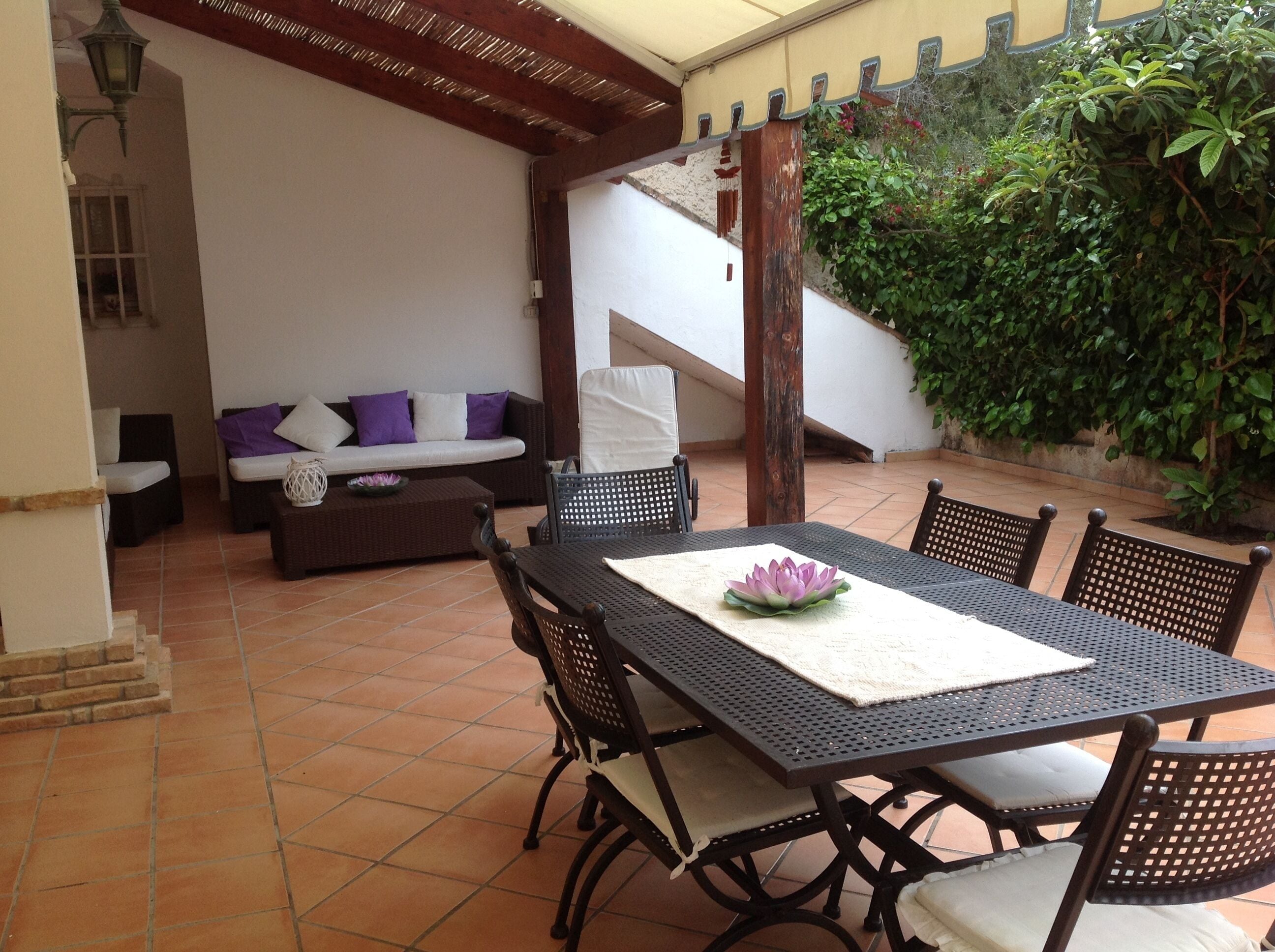 Un patio exterior con una mesa de comedor, sillas, un sofá y una escalera que conduce a una zona cubierta.