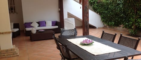 An outdoor patio with a dining table, chairs, a sofa, and a staircase leading to a covered area.