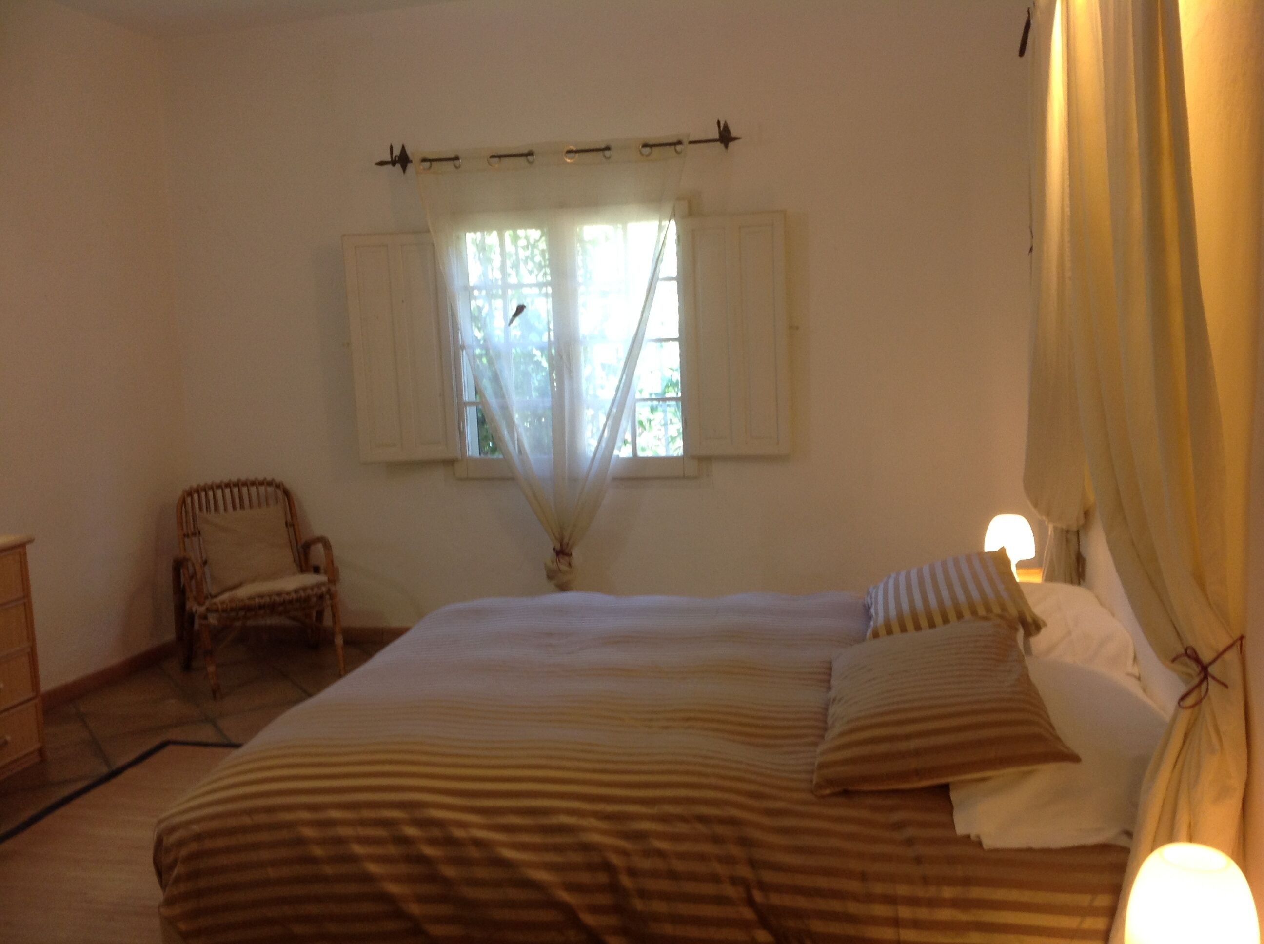 A bedroom with a large bed, a chair, and a window with curtains.