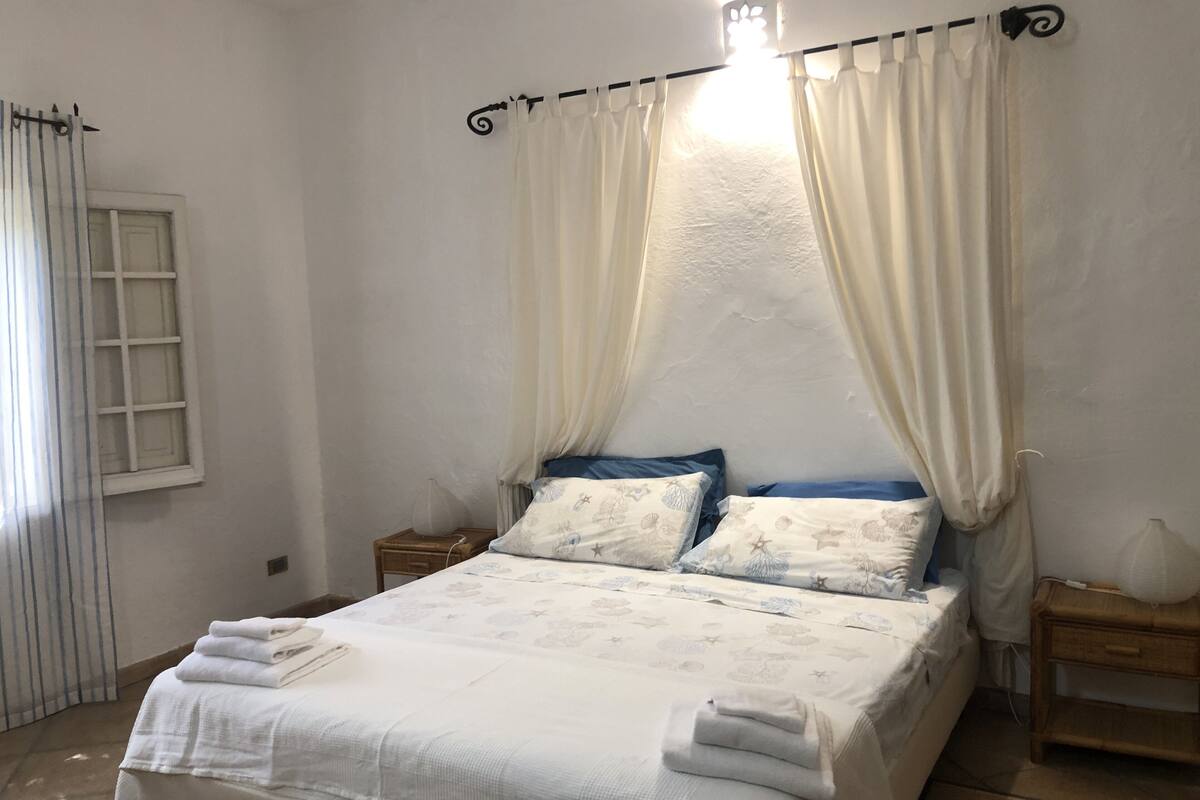 A bedroom with a bed, two bedside tables, a window, and curtains.