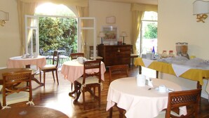 A dining area with round tables covered in pink tablecloths, wooden chairs, and a view of greenery outside. - Hotel Sant'Andrea (Ravenna)