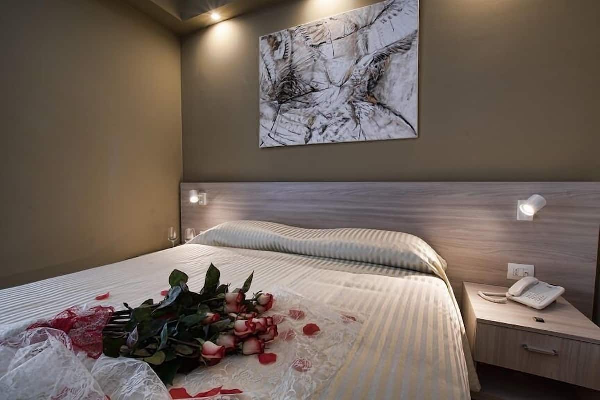 A neatly made bed with a bouquet of flowers and rose petals, a bedside phone, and a wall-mounted abstract painting.