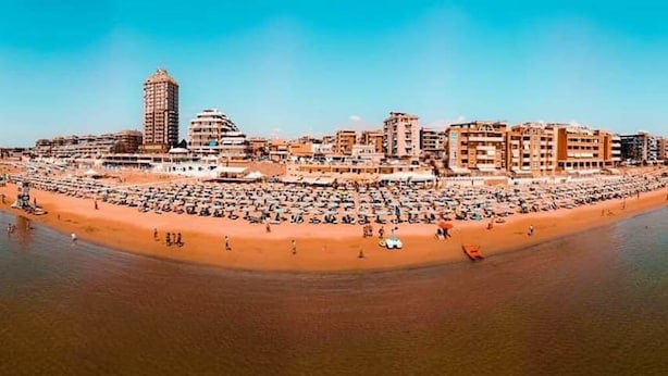 Un paysage urbain côtier avec une vaste plage, de nombreux bâtiments et un ciel dégagé.