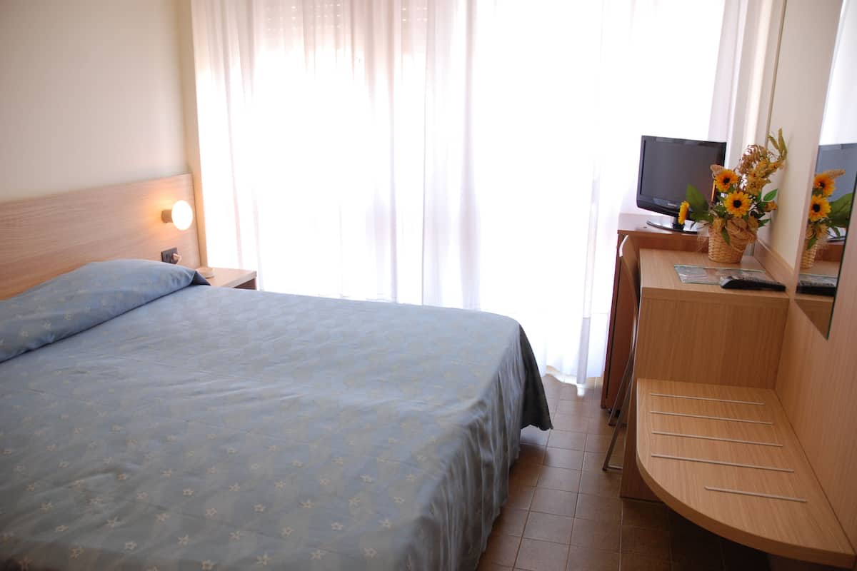 A hotel room with a bed, a desk, a television, and a window with curtains.