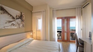 Une chambre d’hôtel avec un lit, un bureau et une vue sur la mer, visible à travers une porte vitrée.