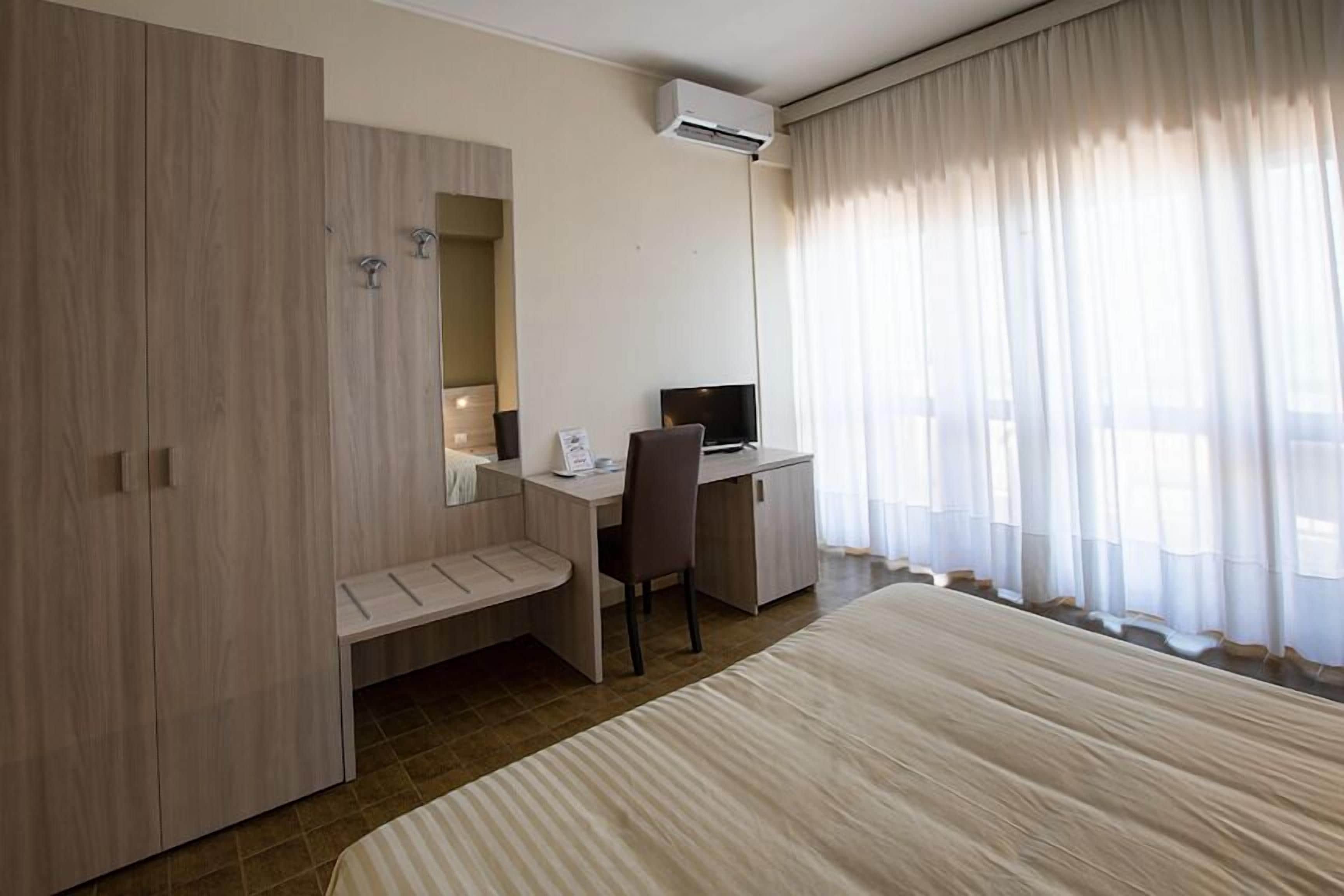 A hotel room with a bed, a desk, a chair, a wardrobe, and a window with curtains.