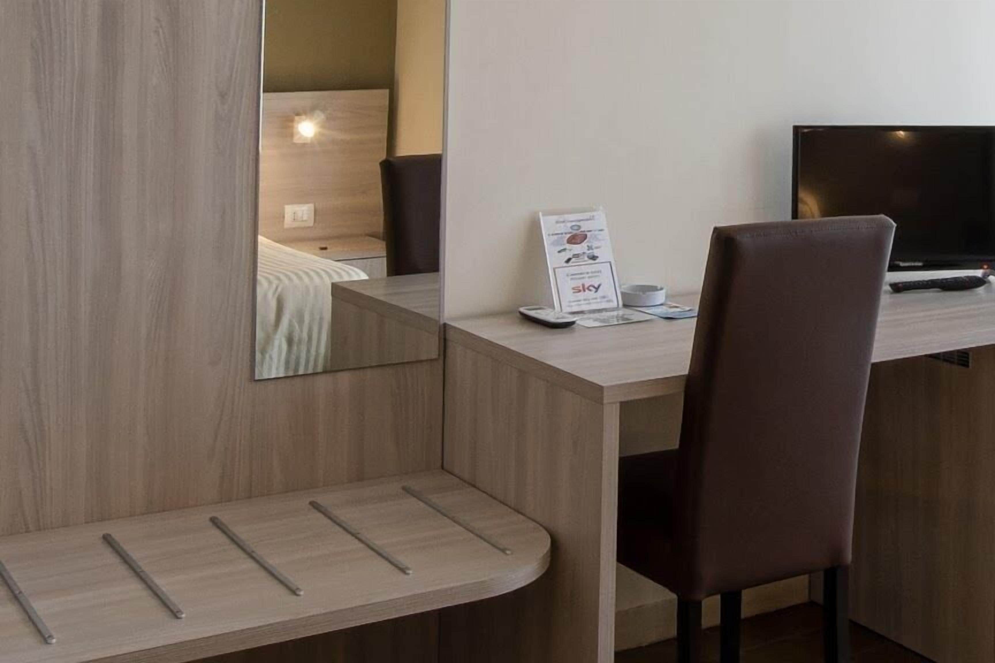Ein modernes Hotelzimmer mit einem Holztisch, einem Sessel, einem Flachbildfernseher und einem Bett mit Kopfteil.