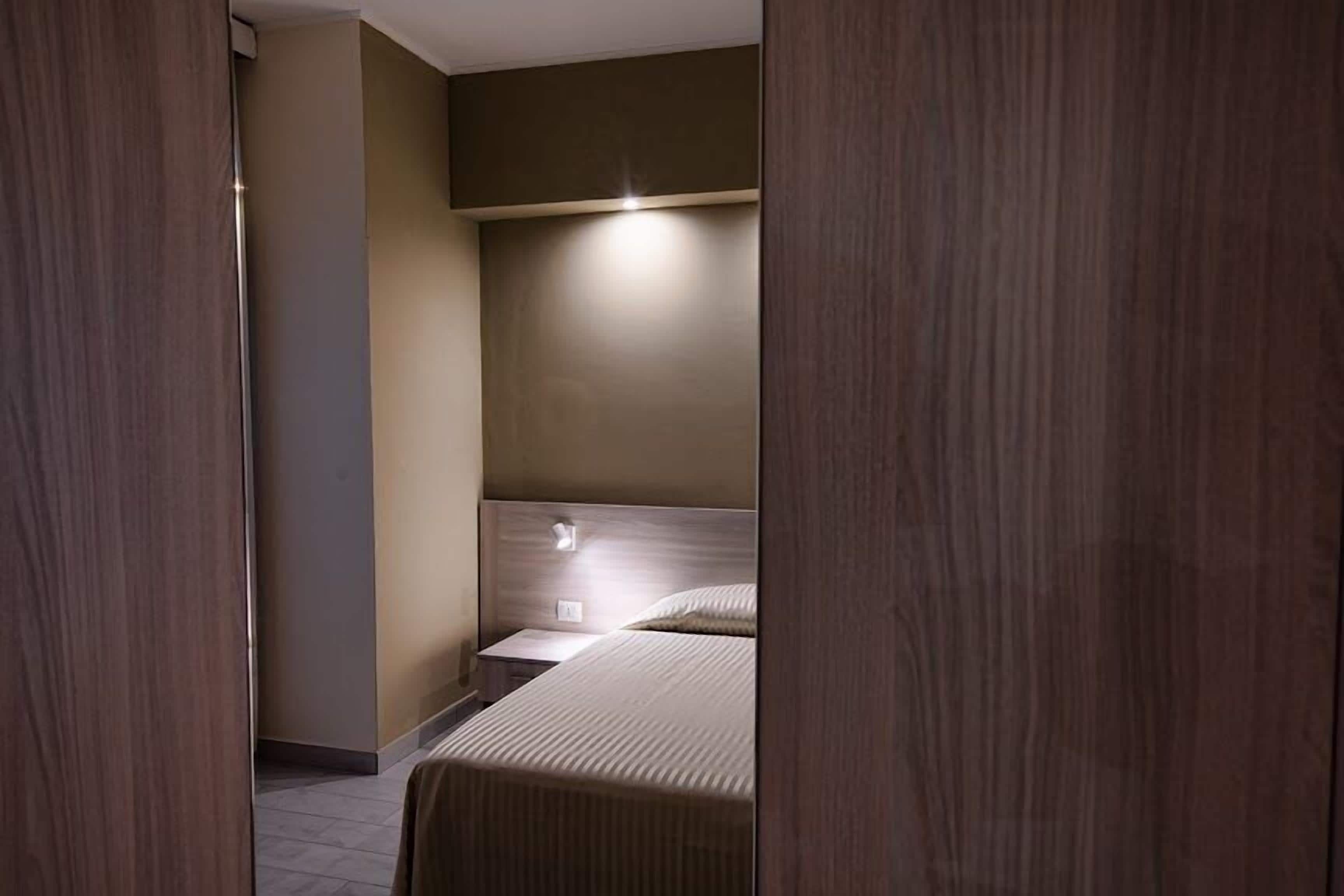 Una habitación de hotel moderna con una cama, mesitas de noche y una lámpara fijada a la pared.