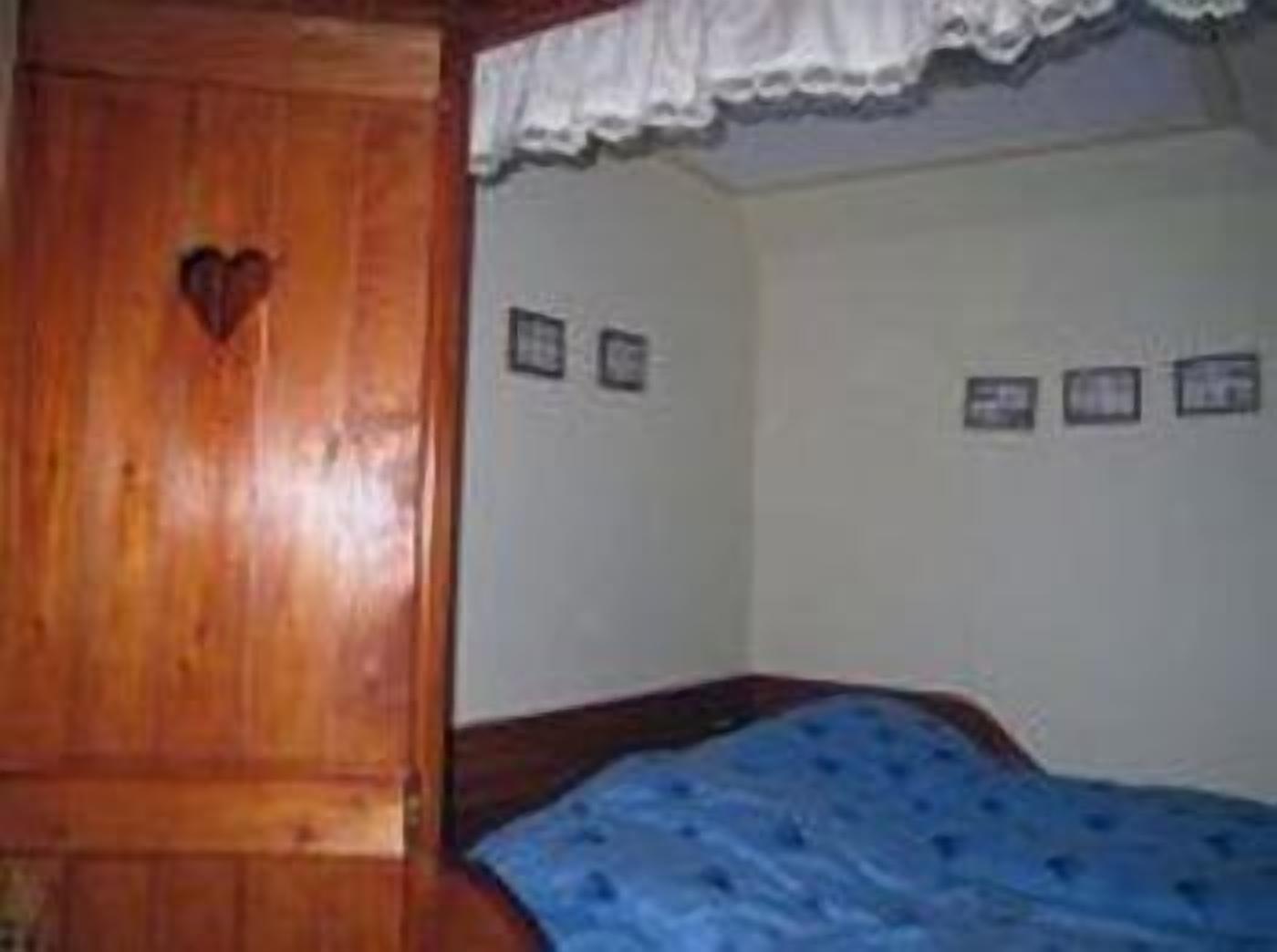 Un dormitorio con un armario de madera, una cama con manta azul y tres cuadros en la pared.
