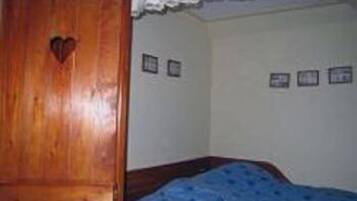 Un dormitorio con un armario de madera, una cama con manta azul y tres cuadros en la pared.