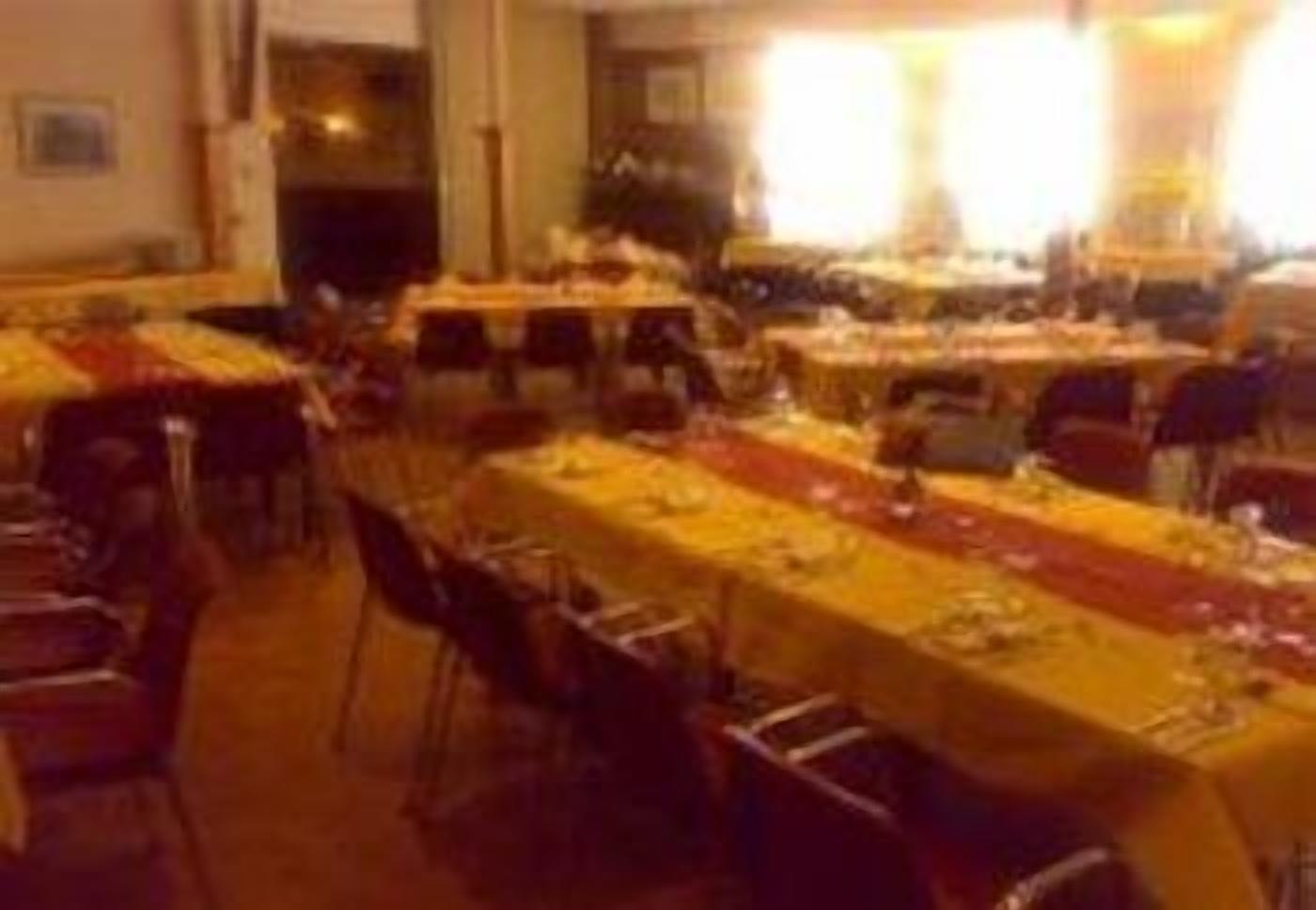 Un salón de banquetes con varias mesas dispuestas para comer, sillas organizadas alrededor de cada una y un camino de mesa largo en el centro.