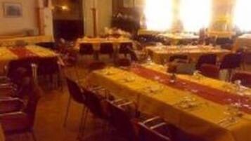 Un salón de banquetes con varias mesas dispuestas para comer, sillas organizadas alrededor de cada una y un camino de mesa largo en el centro.