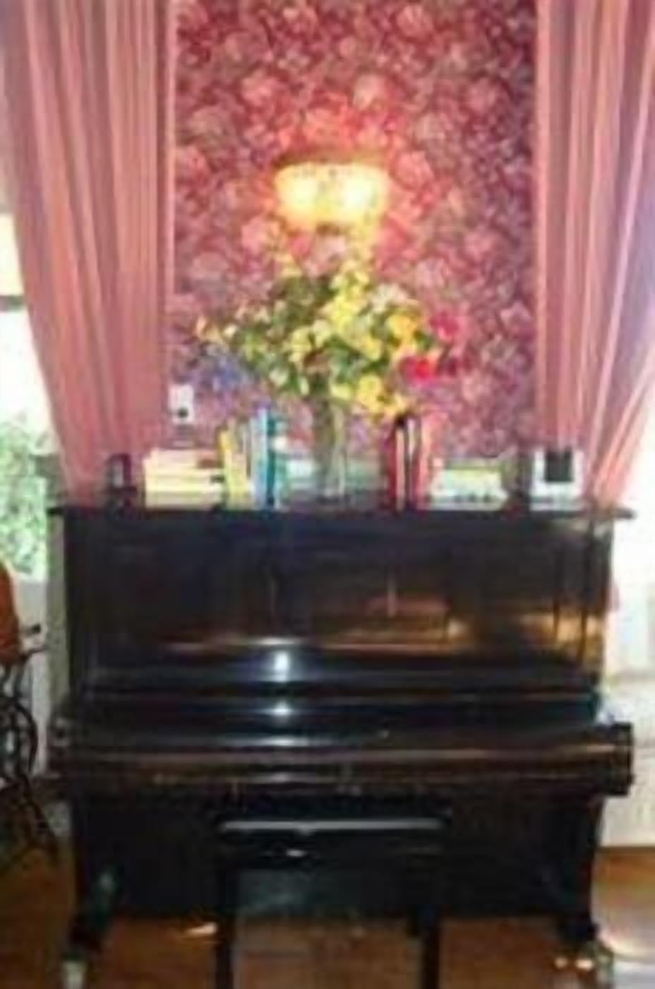 Un piano en una habitación con papel tapiz floral y cortinas rosadas.