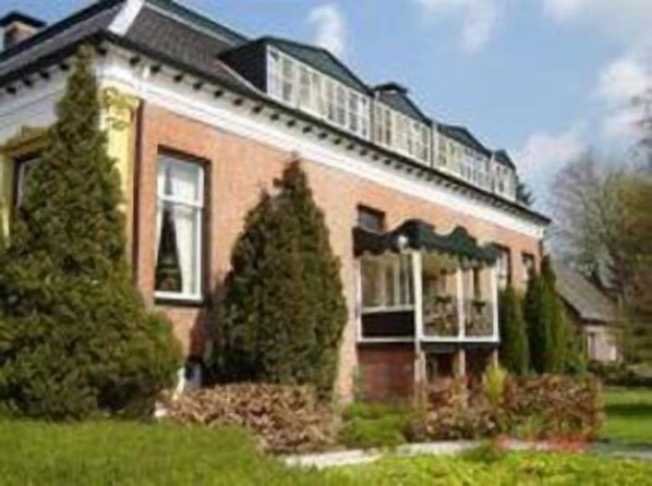 A two-story house with a brick facade, large windows, and a porch with a green awning.