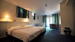 Habitación de hotel con una cama grande, un escritorio y una silla. Hay una ventana con cortinas, una lámpara y un cesto de basura.