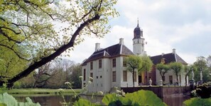 A historic building with a prominent tower, surrounded by lush greenery and a calm body of water. - Hostel Herberg de Esborg (Scheemda)