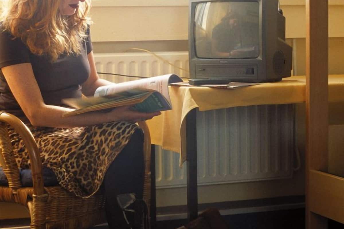 A person sitting on a chair reading a book near a television on a table.