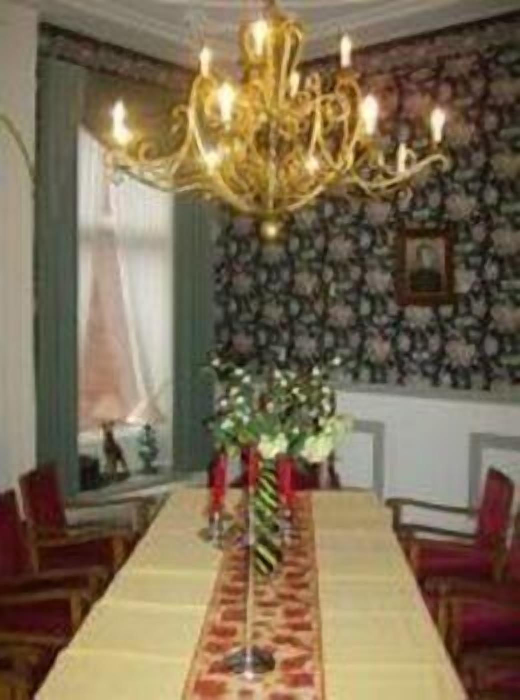 Ein Esszimmer mit einem langen Tisch, roten Stühlen, einer Pendelleuchte und floralem Wandpapier.