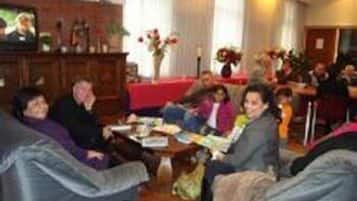 Un groupe de personnes est assis autour d’une table dans une pièce dont un mur est en briques et qui est recouverte d’une nappe rouge.
