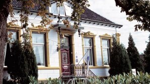 Un edificio de dos pisos con fachada blanca, detalles dorados y una entrada central con puerta roja.