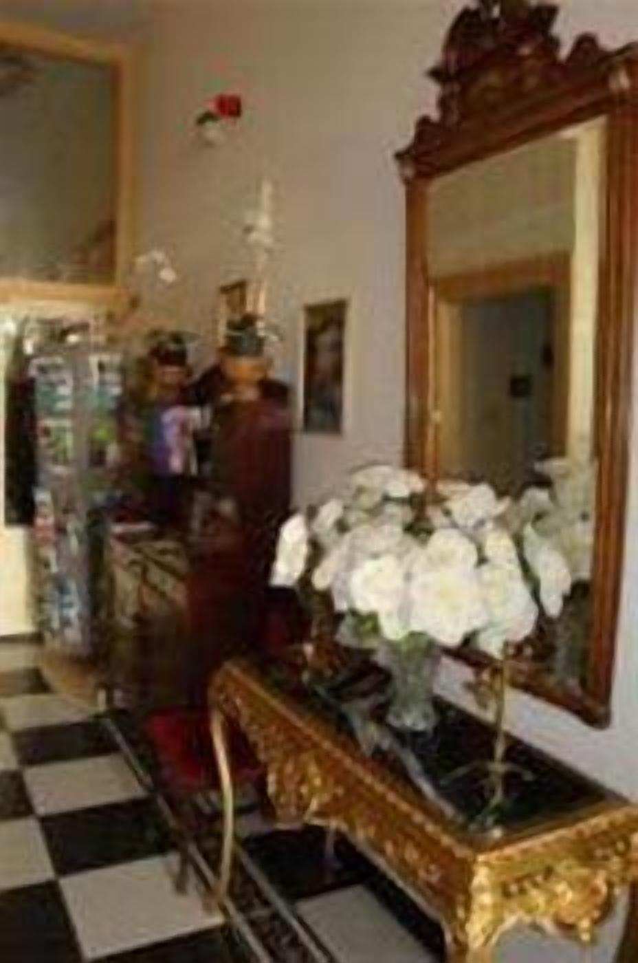 A room with a checkered floor, a mirror, a vase with white flowers, and a dresser with a mirror.
