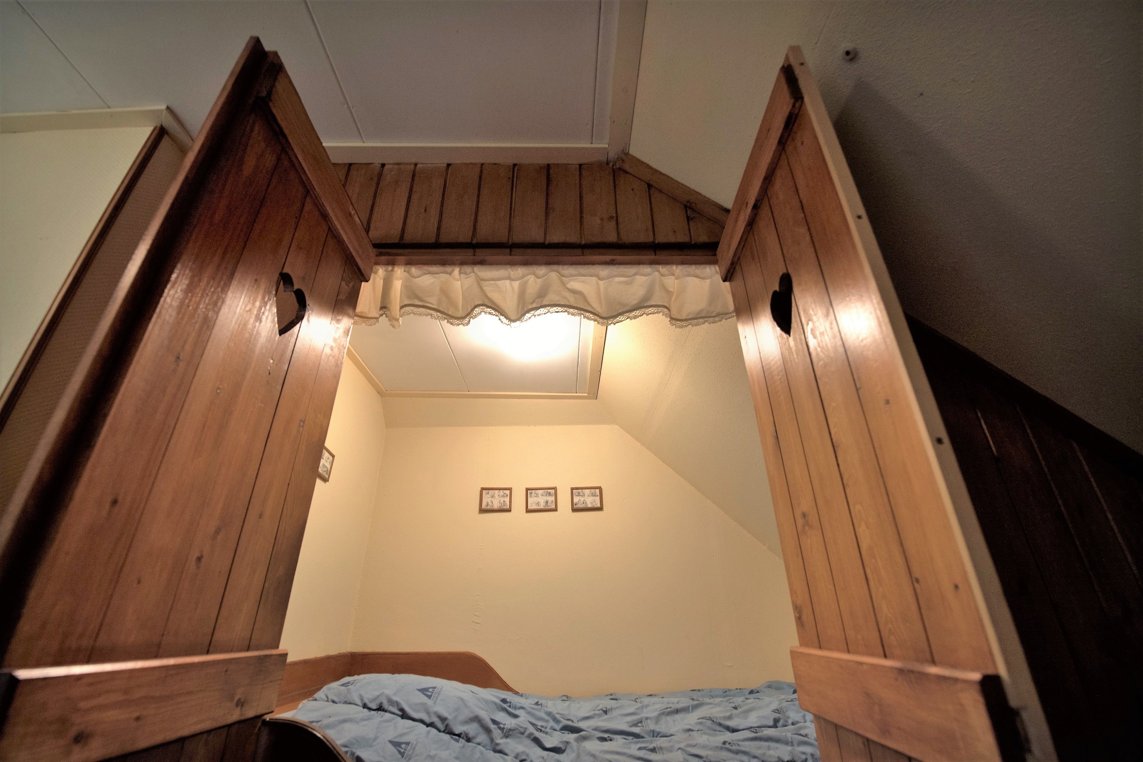 A bedroom with a sloped ceiling, wooden headboard, and a bed with a blue bedspread. There are three framed pictures on the wall.