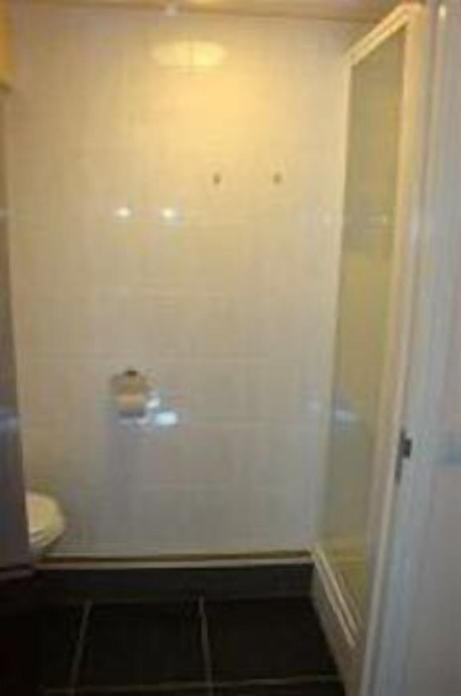 A small, enclosed shower area with a glass door, a toilet, and a tiled floor.