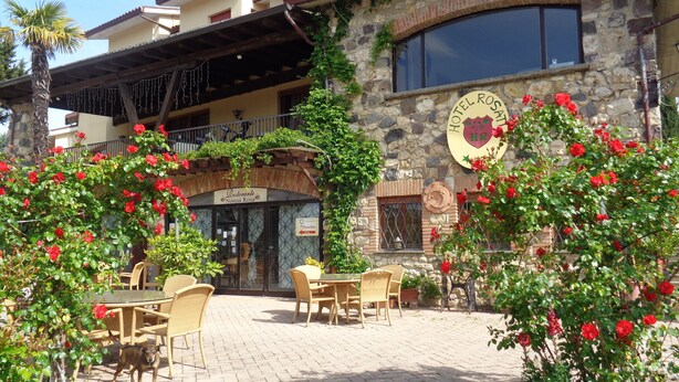 Un restaurante con terraza, paredes de piedra y flores rojas.
