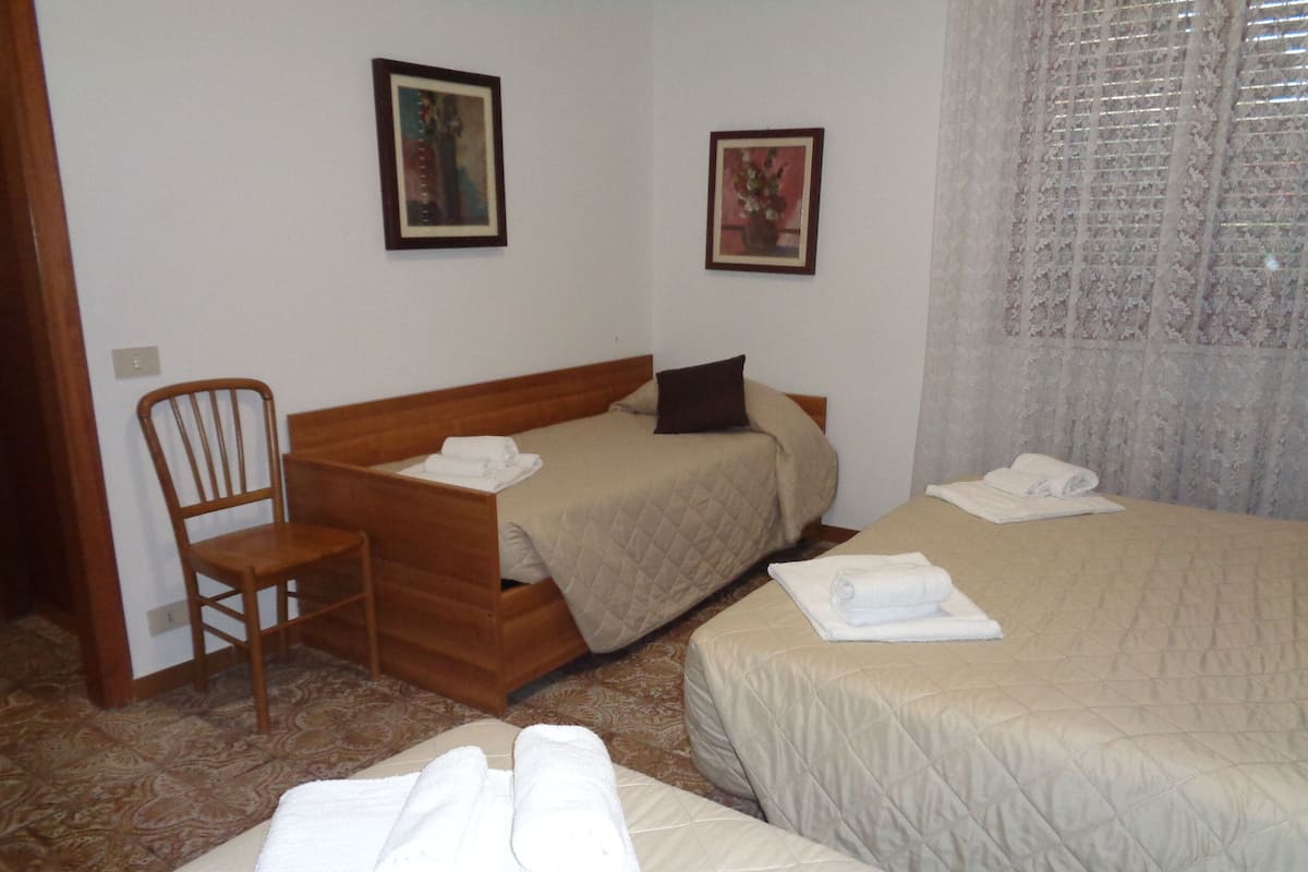 A hotel room with two beds, a wooden chair, and two framed pictures on the wall.