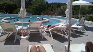 Un área de piscina con sillones de descanso y sombrillas, rodeada de árboles.