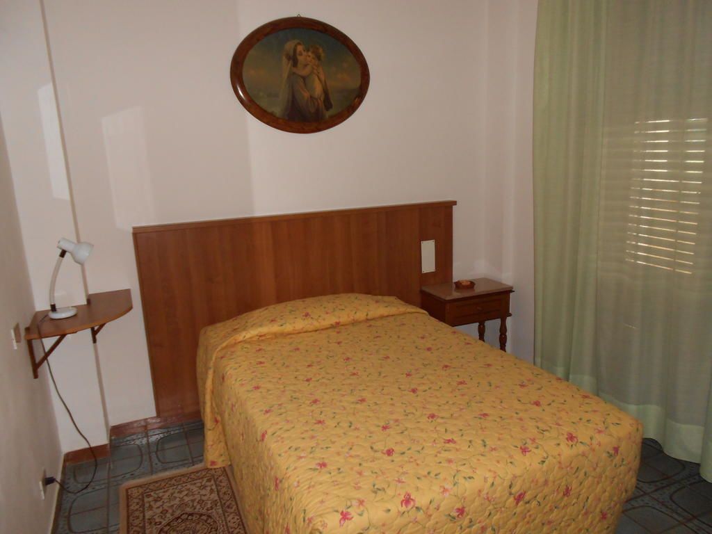 A bedroom with a wooden headboard, a bed with a floral bedspread, a bedside table with a lamp, and a painting on the wall.