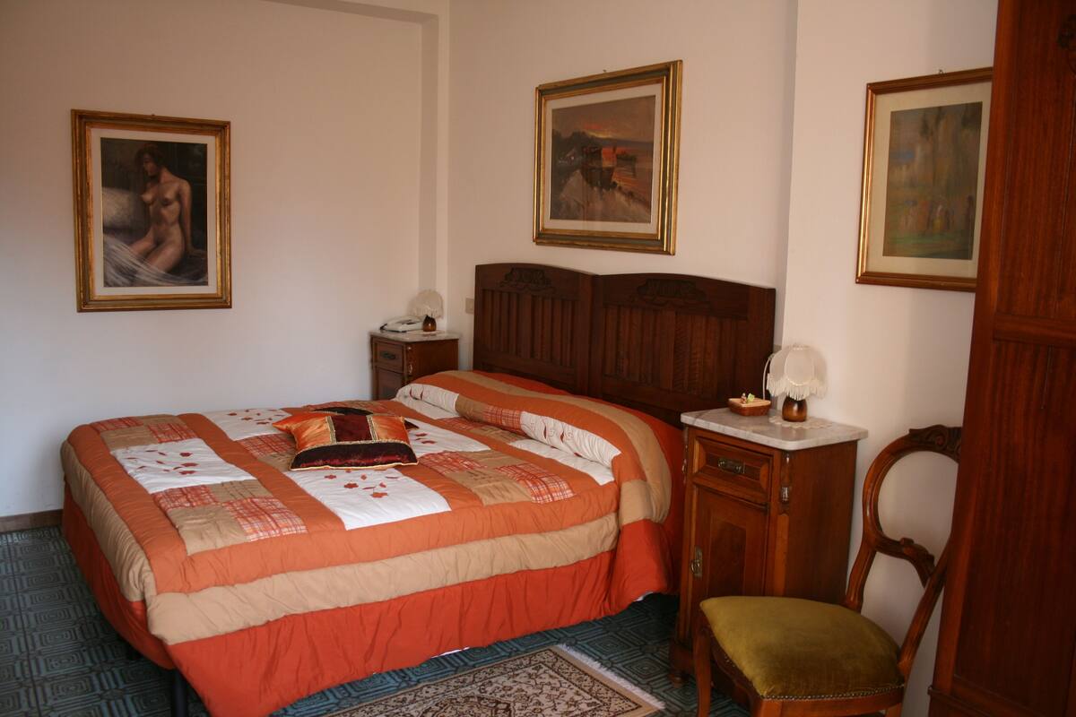 A bedroom with a large bed, a wooden nightstand, a chair, and three framed pictures on the wall.