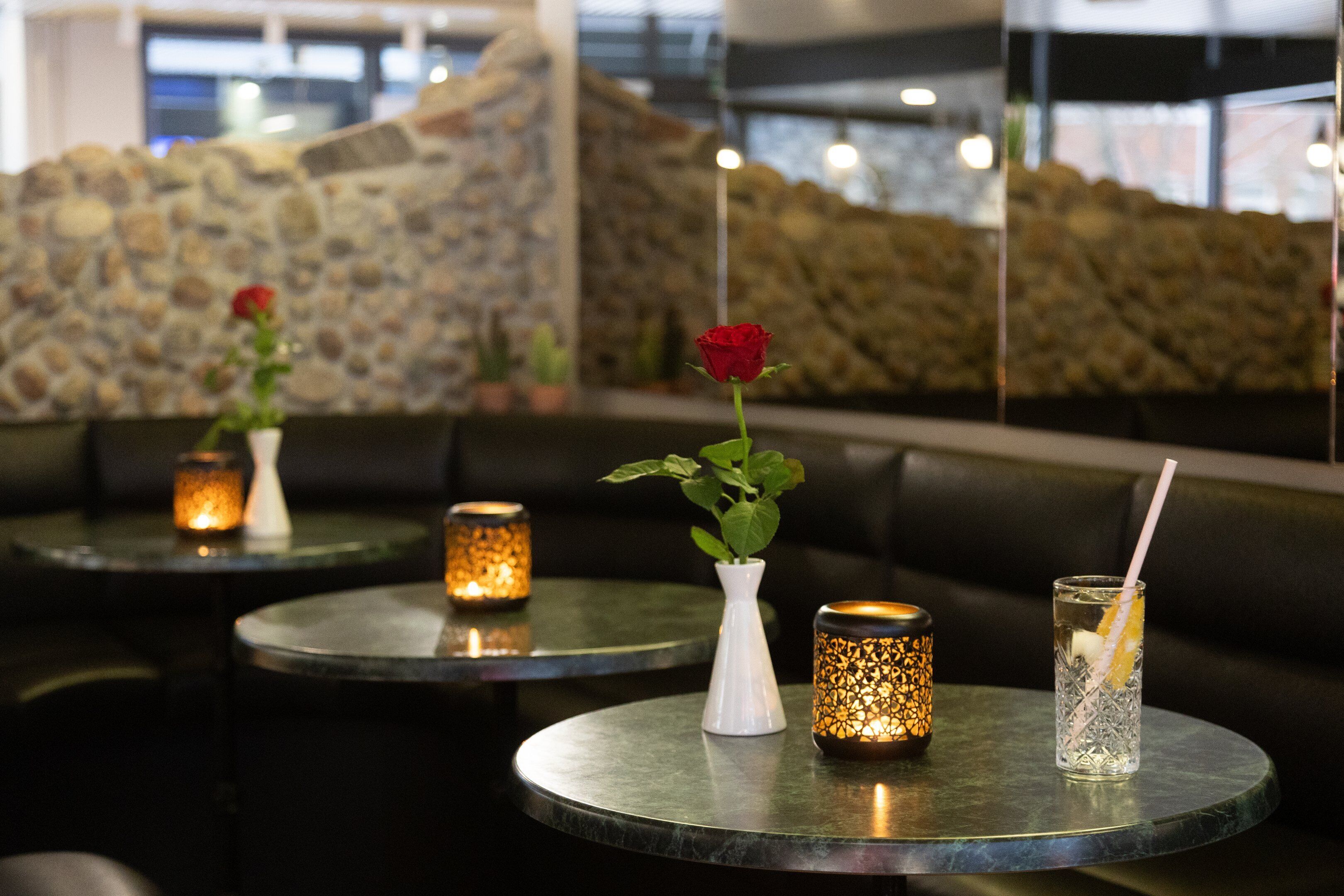 Interno di un ristorante con tavoli rotondi, candele e un vaso con una rosa.
