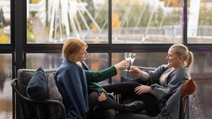 Dos personas sentadas en un sofá mirando por una ventana con vistas a un puente y árboles.