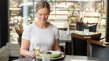 A person seated at a table with a plate of food and a glass of white wine.