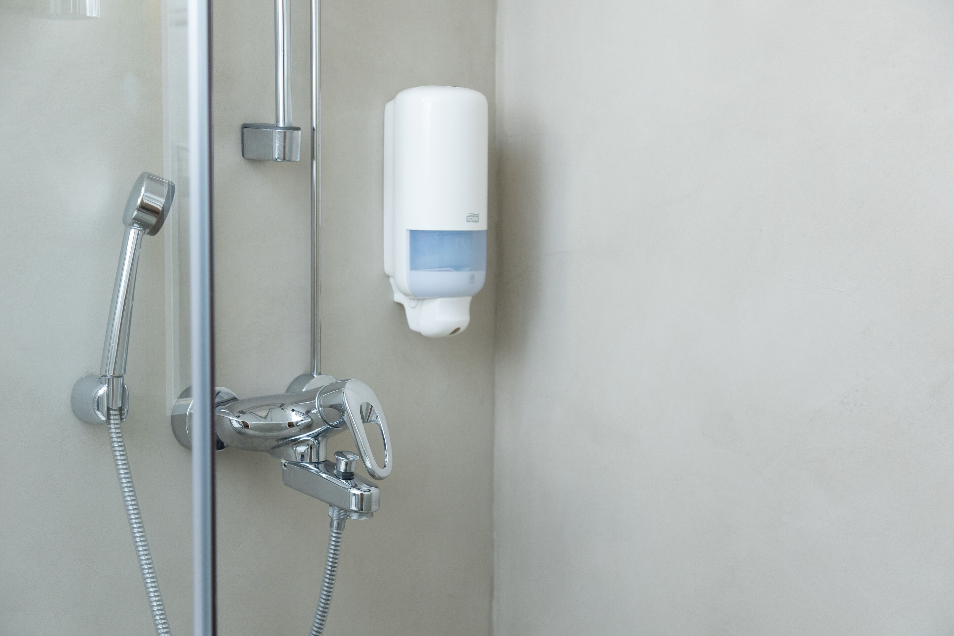 Ducha con cabezal de ducha de mano, dispensador de jabón en la pared y grifo de cromo.