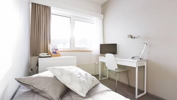 A hotel room with a bed, a desk, a chair, a computer, and a window with curtains.