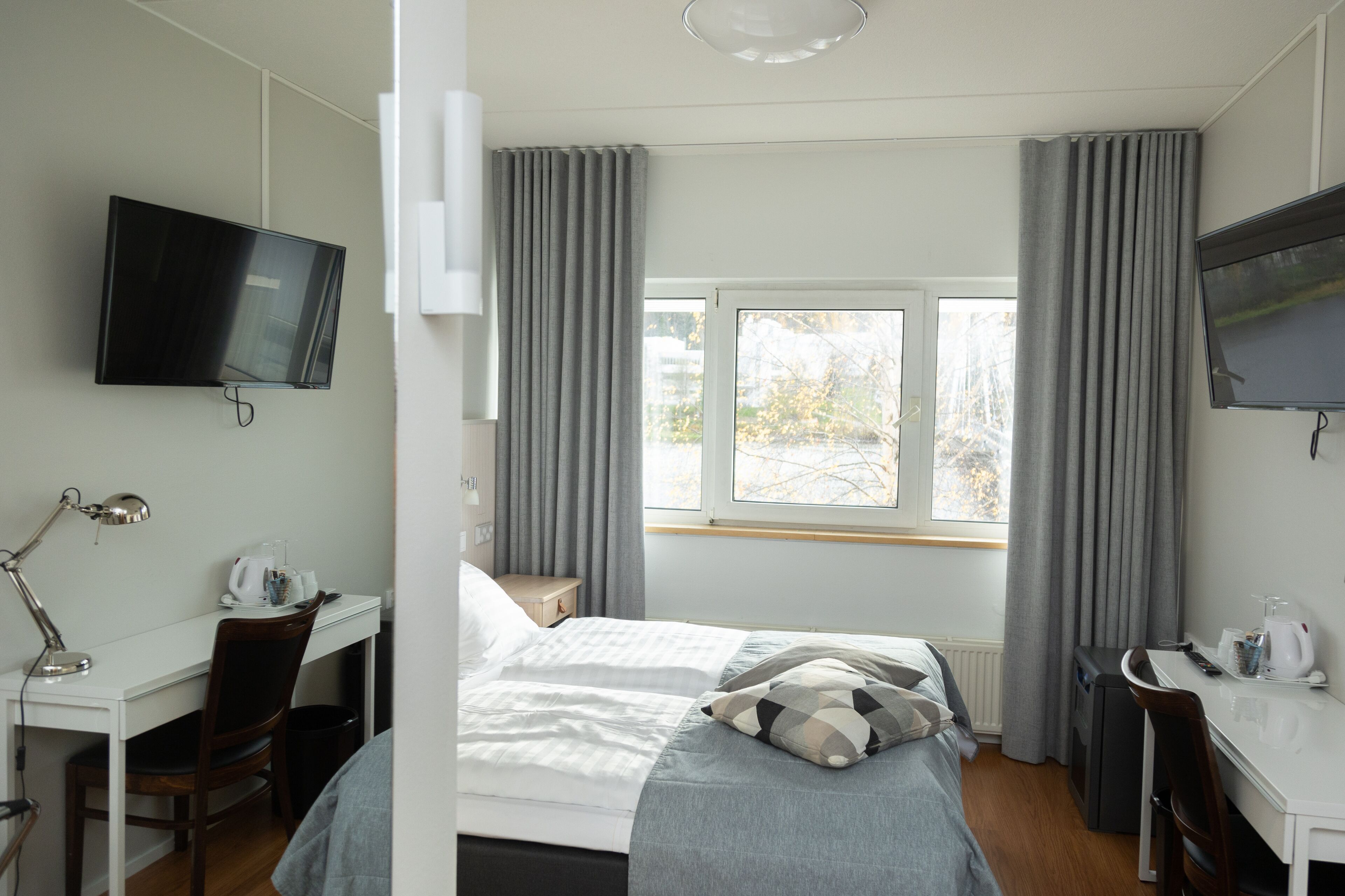 Una habitación de hotel moderna con una cama, un escritorio, una silla, un televisor y una ventana con cortinas.