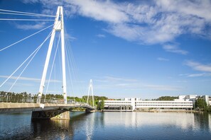 A modern bridge with white cables and a concrete deck over a calm river, with a building in the background.