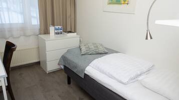 Een slaapkamer met een bed, nachtkastje, stoel, bureau en een raam met gordijnen.
