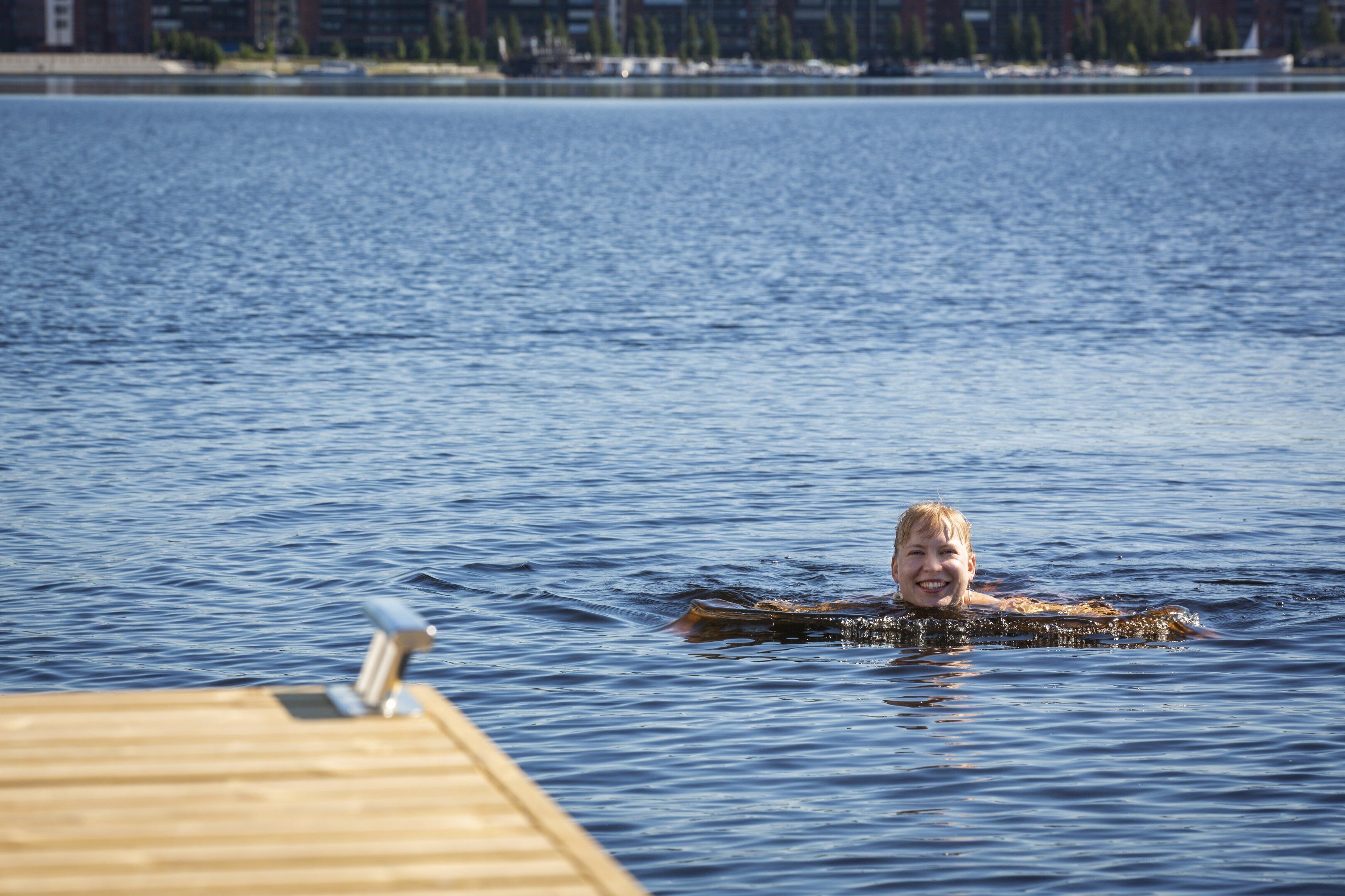 A wooden dock extending into a calm body of water with a person swimming.