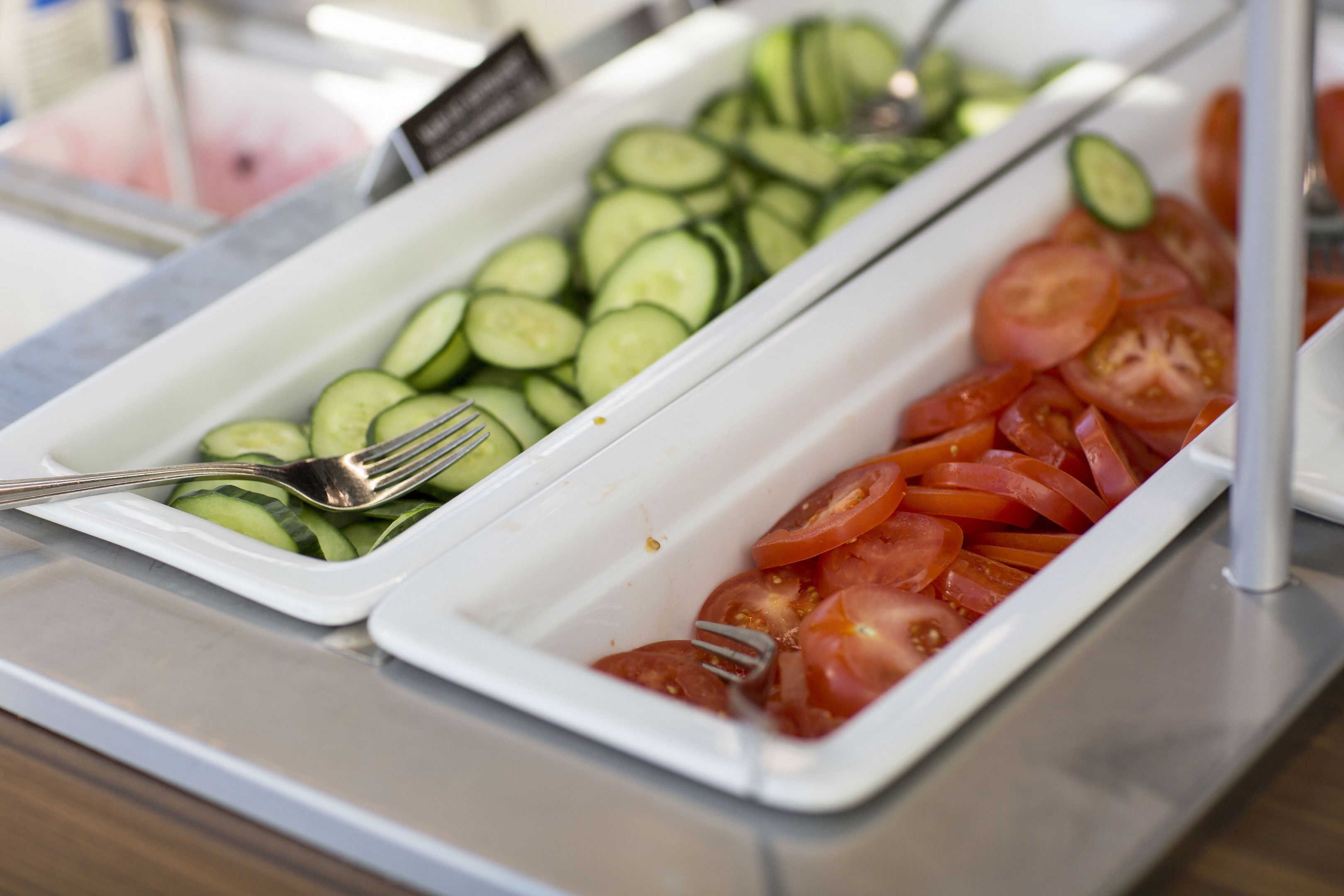 A buffet with trays of sliced cucumbers and tomatoes.
