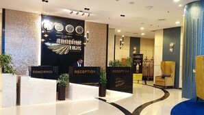 Zona de recepción de un hotel con diseño moderno, que incluye un mostrador de recepción, un reloj que muestra múltiples zonas horarias y un cartel de recepción.