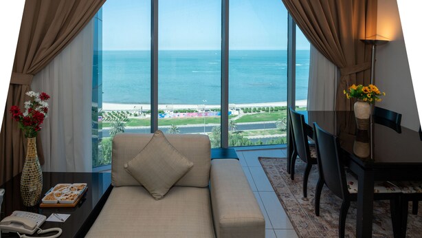 Una habitación con un sofá, una mesa de comedor y sillas, un florero con flores, y vista al mar.