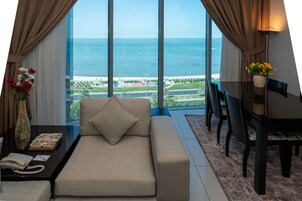 Una habitación con un sofá, una mesa de comedor y sillas, un florero con flores, y vista al mar.