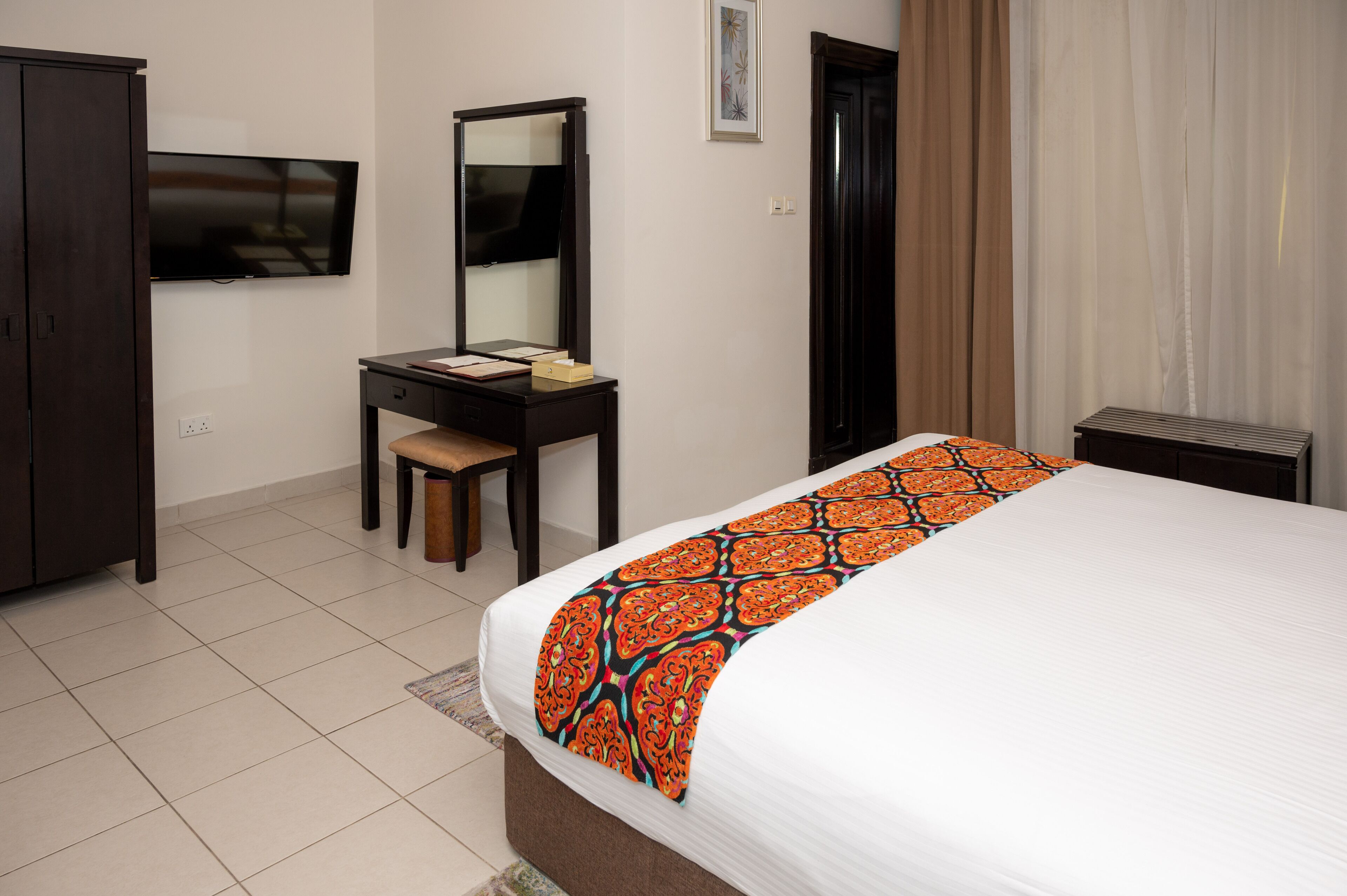 A hotel room with a bed, a desk, a chair, a television, and a wardrobe.