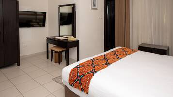 A hotel room with a bed, a desk, a chair, a television, and a wardrobe.
