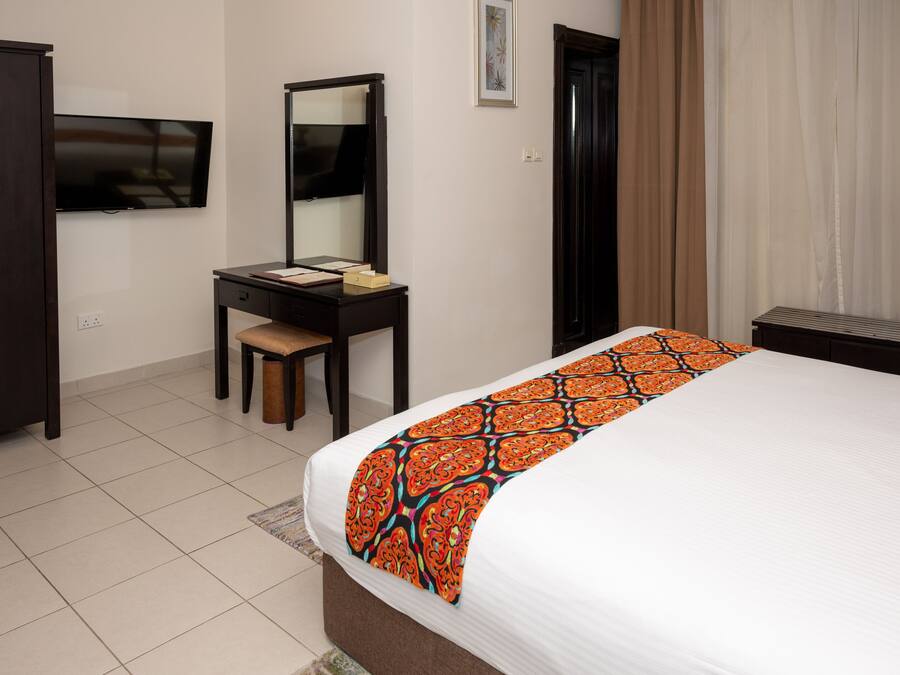 A hotel room with a bed, a desk, a chair, a television, and a wardrobe.