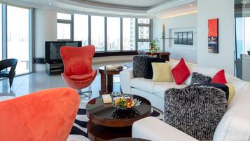 Una sala de estar moderna con un televisor de pantalla plana grande, un sofá blanco con cojines de colores, un sillón rojo y una mesa de centro con un arreglo floral.