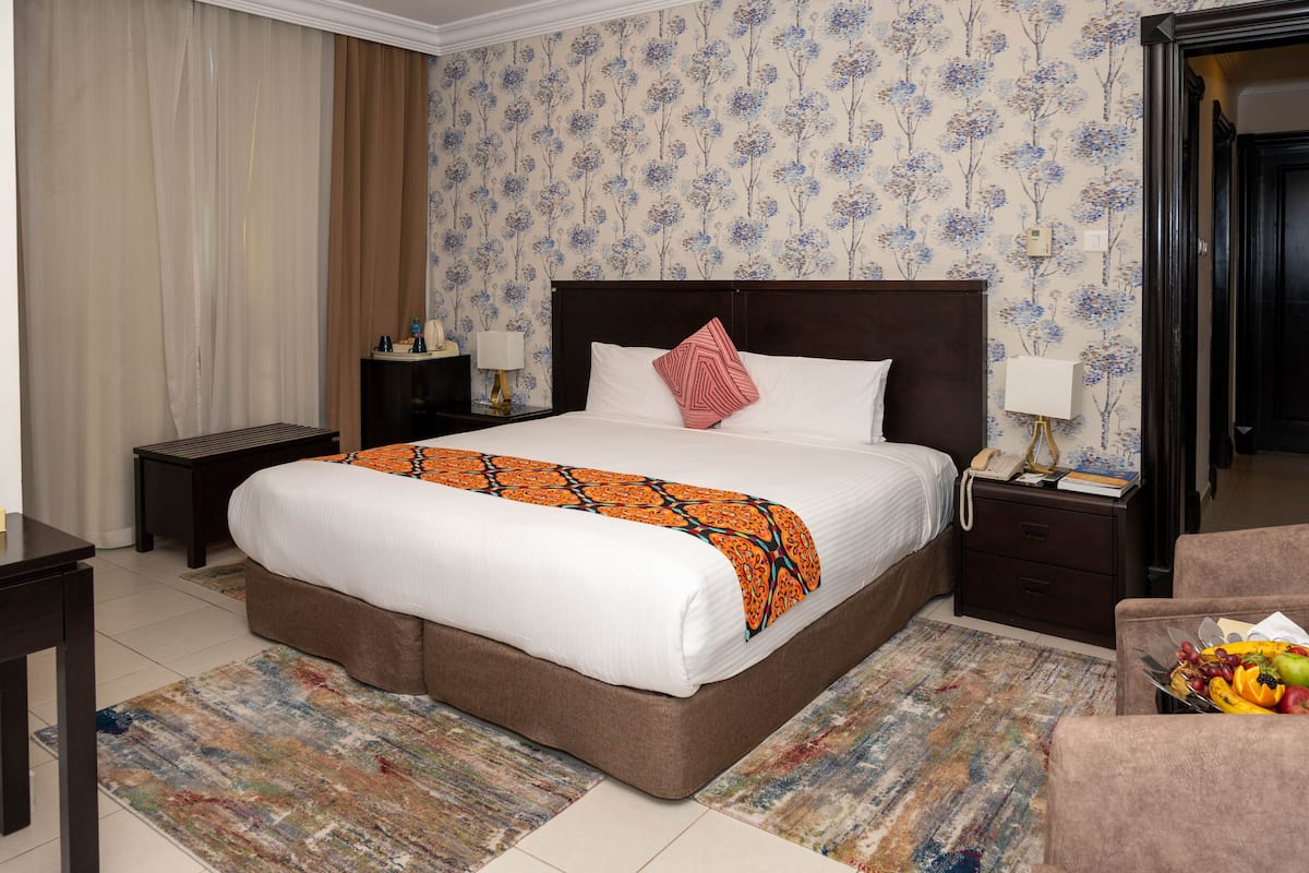 Une chambre d’hôtel avec un grand lit, une table de chevet, une chaise et un panier de fruits.